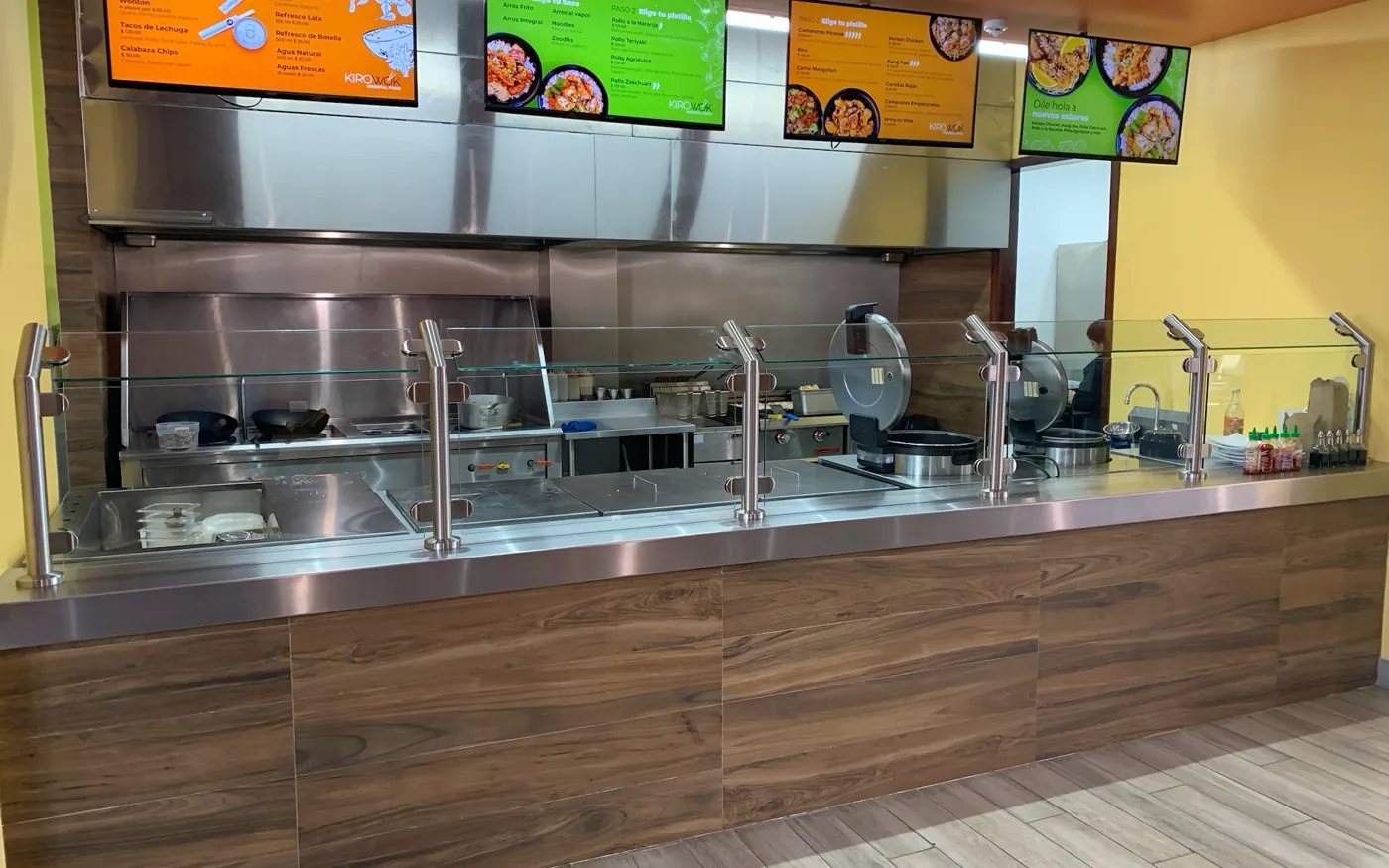 Barra de despacho en acero inoxidable con antiestornudo de cristal, instalada y en operación en un local de comida